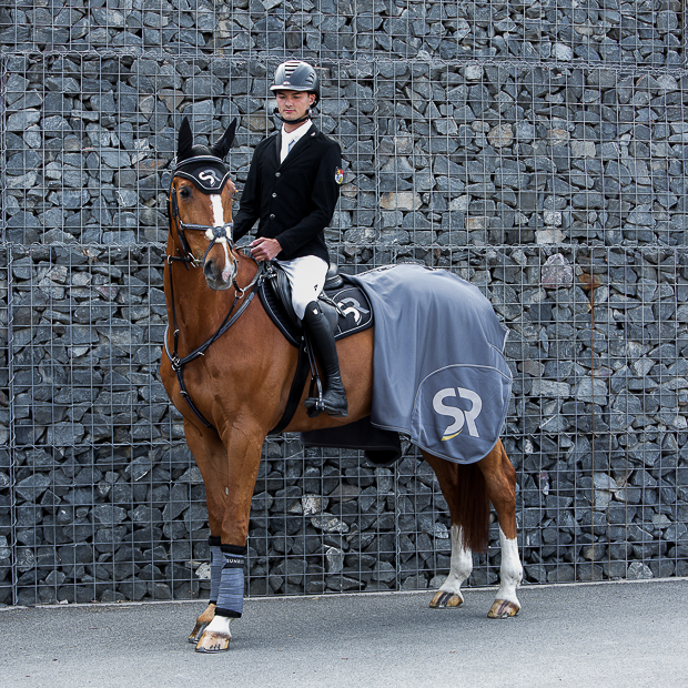 black silver sr line set with jumping saddle pad, fly earnet, bandages and cooler rug by sunride under a saddle on a horse with rider 