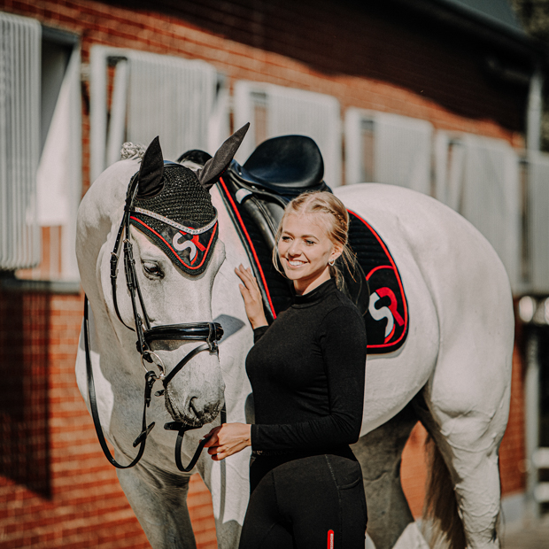 set of breathable dressage saddle pad red and black exclusive line with fur on withers and matching earnet on a horse with rider