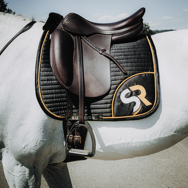 schwarz goldene dressurschabracke mit sr logo am pferd dressurschabracke in schwarz mit goldener umrandung sowie goldenem sr logo von sunride am pferd