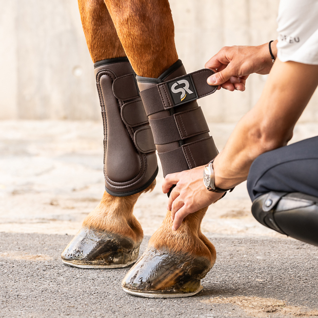 brown dressage leather boots from leather and neoprene inside with elastic velcro closures on the horse leg while attaching by rider