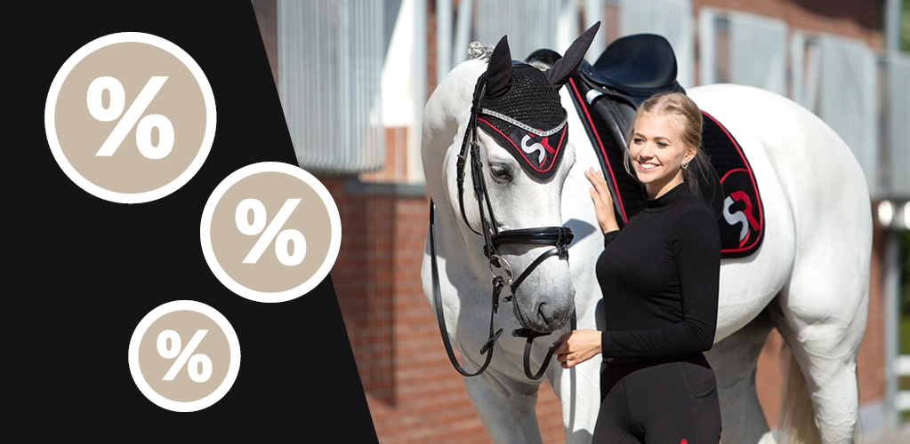 Sale Eine Reiterin steht neben einem Pferd mit schwarz roter Schabracke und passender Fliegenhaube mit SR Logo im Hintergrund ist ein Stall