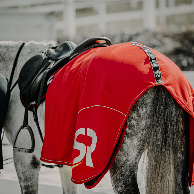 red boston cooler rug made of softshell and fleece with reflecting sr logo by sunride on a horse with saddle