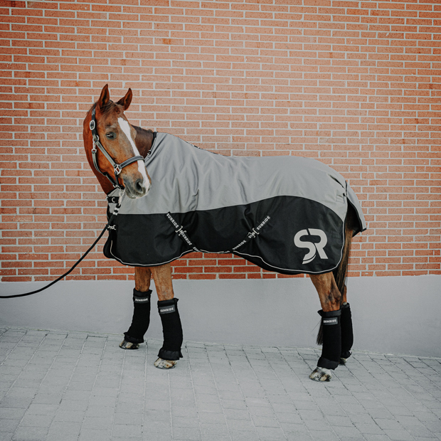 black leather halter dallas and black stable bandages with pads and grey helsinki winter rug with 250 grams filling and reflecting elements and red leather cord halter by sunride on a horse in front of a stable