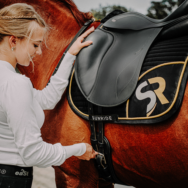black leather dressage girth monaco with silver mounting by sunride on a saddle with horse and rider
