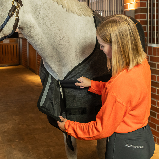 grey wool heating rug st. moritz with three levels of heating and program on a horse in the stable with rider on front closure