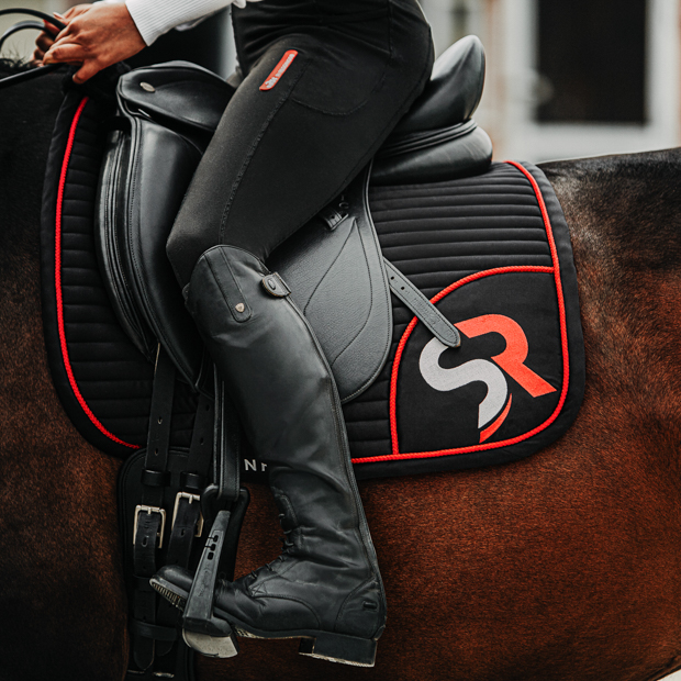 dressurschabracke in schwarz mit roter umrandung sowie rotem sr logo von sunride am pferd