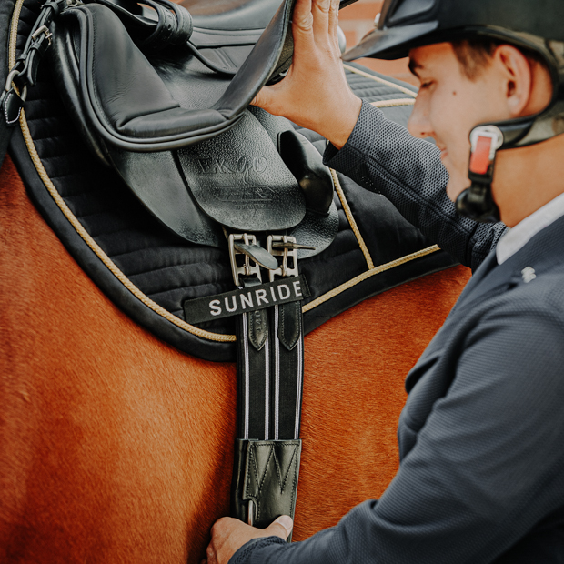 elastic black leather stud guard girth hickstead with silver mounting by sunride on a saddle on horse